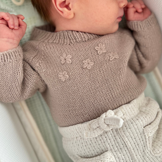 Strikkepakke body til baby i bruk nærbilde av broderte blomster