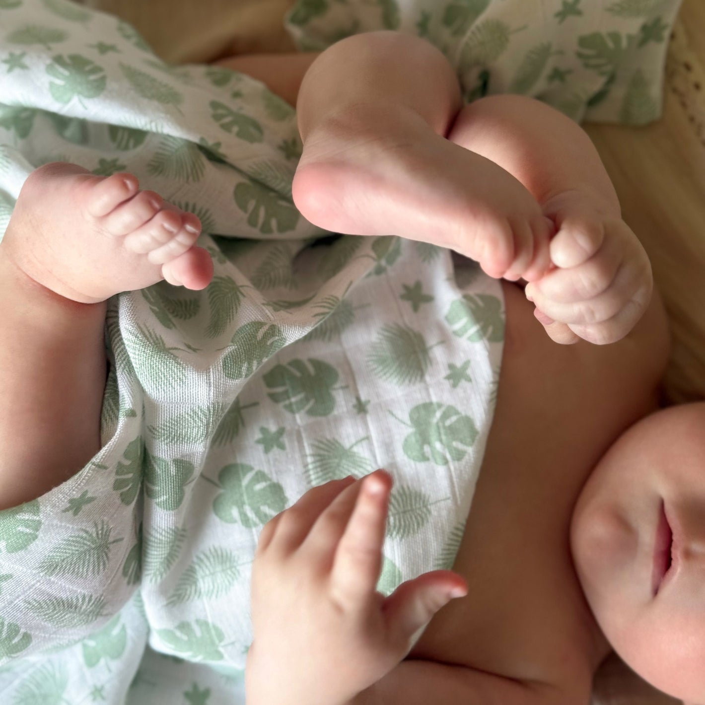 Babypledd, gulpeklut, koseklut fra Summerville Organic i grønn og hvit flerfarget/mønstret i bruk på baby som leker med føttene sine