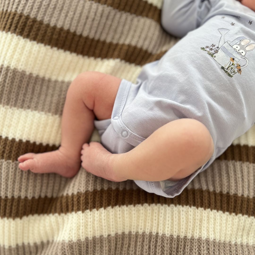 Baby som ligger på Vesleskattens yndlingspledd – babyteppe i 100% kløfri merinoull med halvpatent. Nybegynnervennlig strikkepakke babypledd og vognteppe, lett å strikke. Perfekt som babyens første teppe.