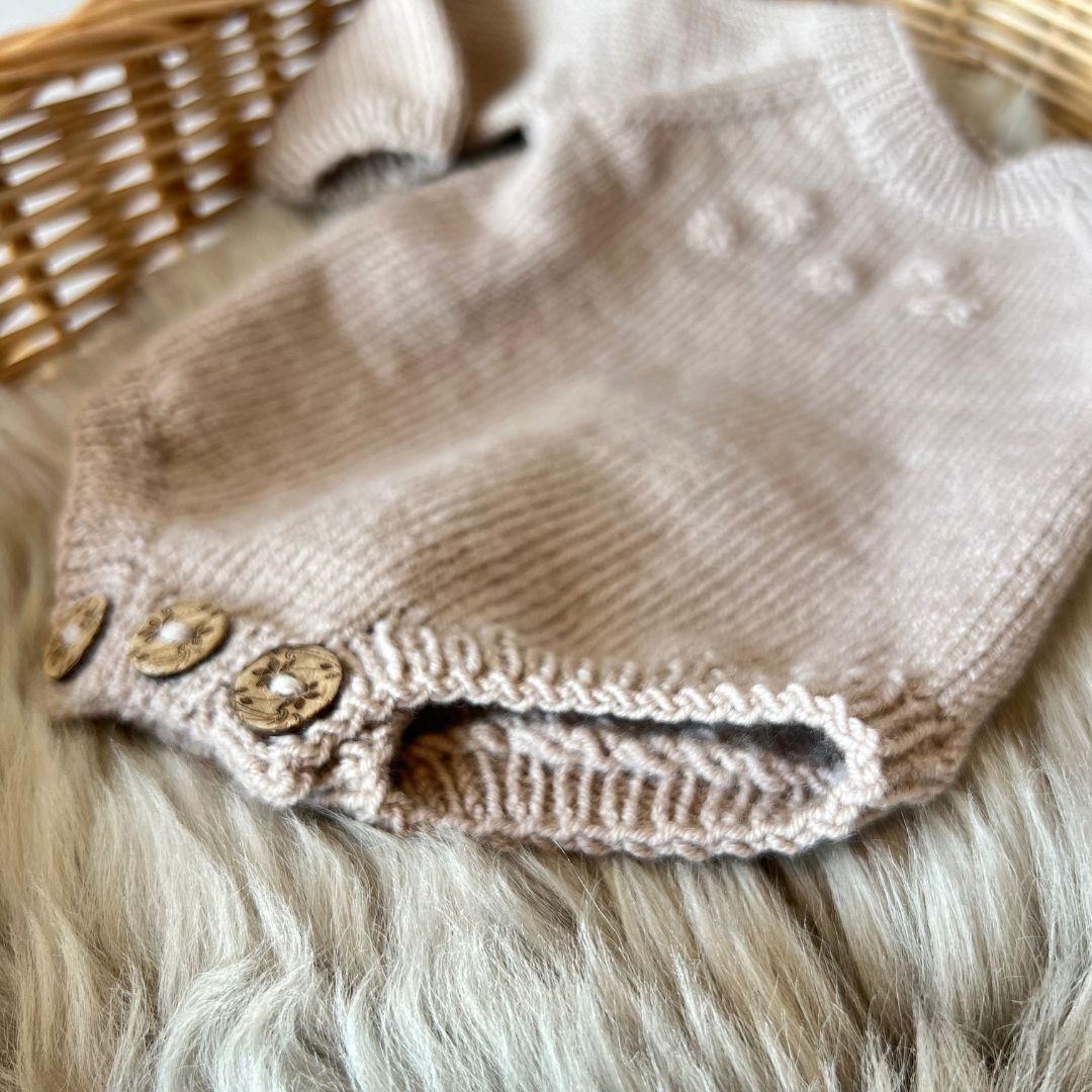 Detaljer på vrangbord rundt lår på strikket baby body – lettstrikket body i 100% merinoull. Strikkepakke blomsterbody med knapper mellom beina for enkelt bleiebytt. Nybegynnervennlig babystrikk med enkel strikkeoppskrift – strikke babygarderoben.