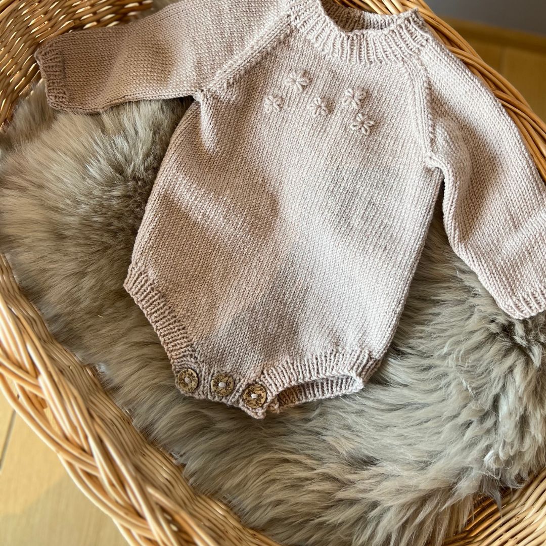 Strikket blomsterbody på saueskinn – lettstrikket body i 100% merinoull med broderte blomster. Strikkepakke blomsterbody kan strikkes med eller uten blomster – nybegynnervennlig babystrikk med enkel strikkeoppskrift. Body er det mest brukte babyplagget – strikk den selv.