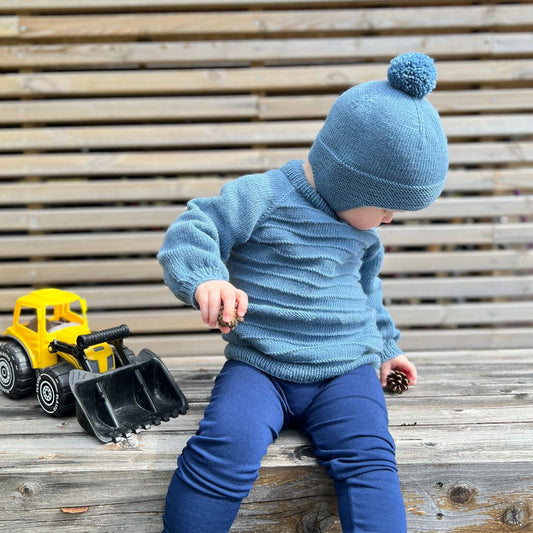 Barn i lek med Vesleskattens drømmesett – genser og lue i 100% kløfri merinoull med rillemønster. Strikkepakke til barnehagebarn 0–3 år, perfekt for aktive barn. Godt som eneste ytterplagg på høst og vår, eller under vinterdressen.