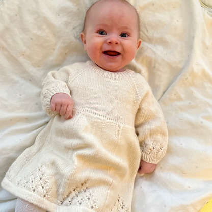 Strikkepakke med Vesleskattens søte kjole - bilde av hvit kjole i bruk på baby. Kjole med hullmønster.