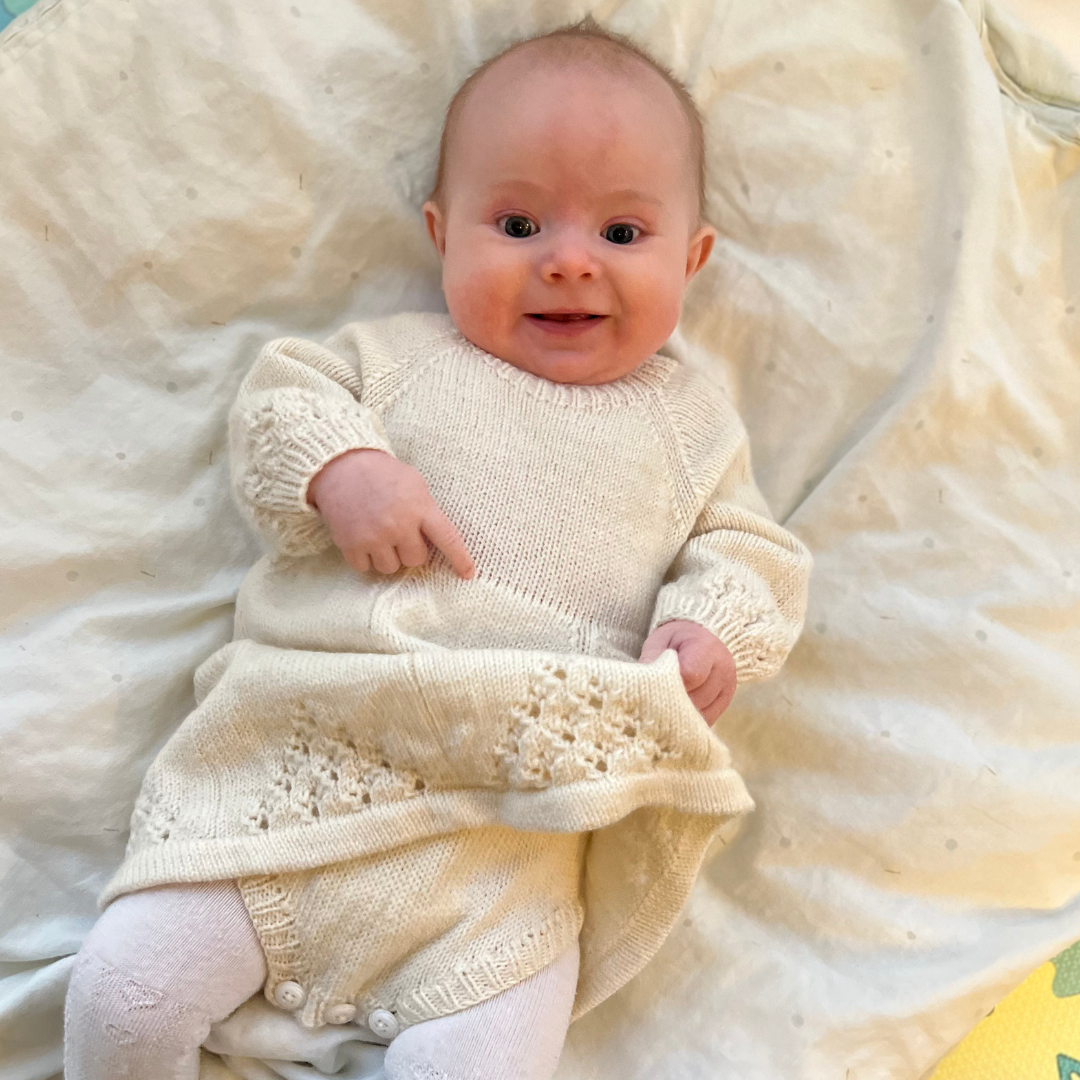 Strikkepakke babykjole med body. Hvit kjole i bruk på baby. Merinoull. Dale Garn.