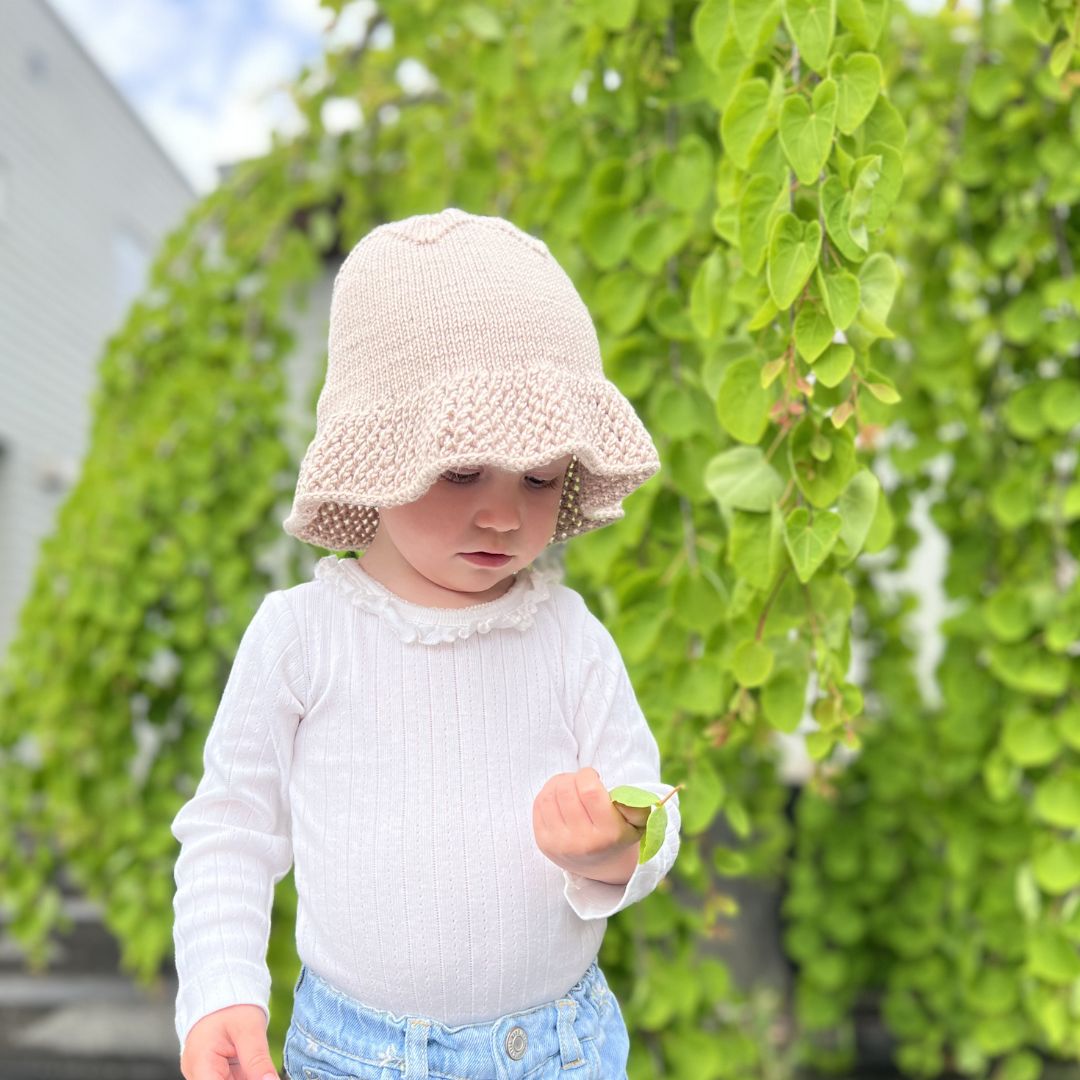 Barn i sand med strikket solhatt – sommerstrikk oppskrift som PDF 6 mnd til 6 år