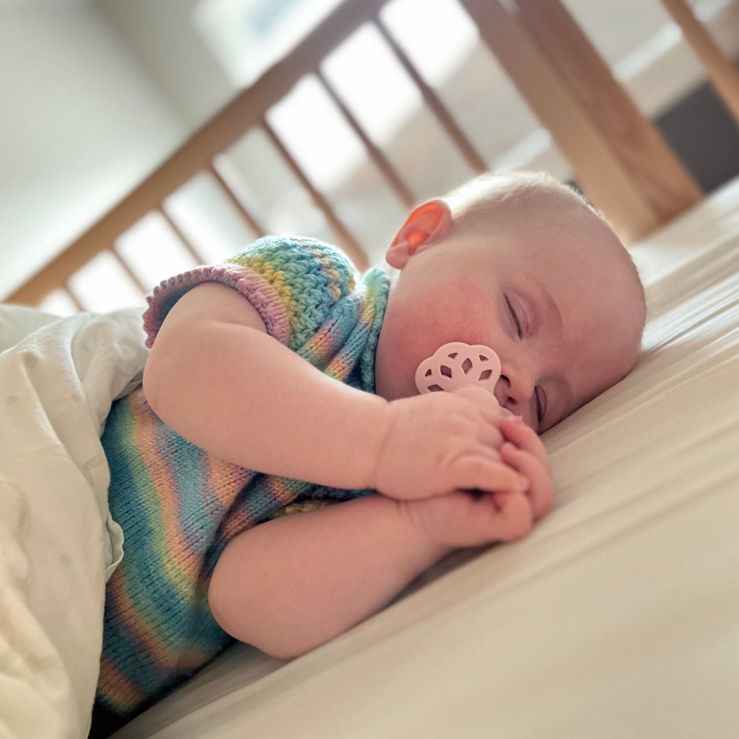 Baby sover i strikket sommerbody – strikkepakke sommerbody som er god å sove i, i 100% merinoull. Strikke sommerbody til baby med knytting i nakken som lufter godt. Merinoull beskytter mot UV-stråler – perfekt sommerbody fra nyfødt til 2 år.