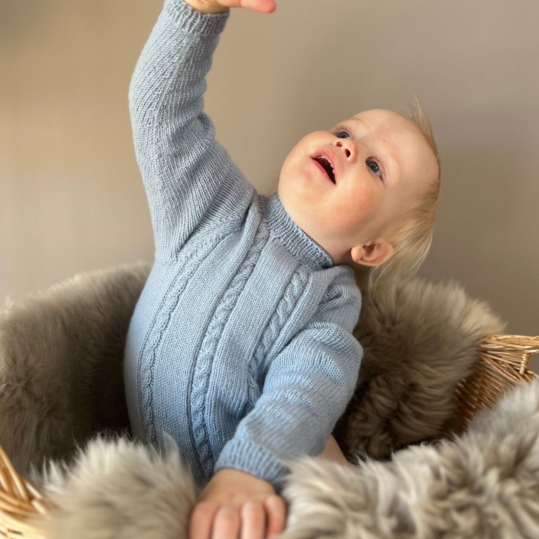 Vesleskattens flettebody i 100% kløfri merinoull med flettemønster – strikkepakke body til baby. Elastisk hals, ingen knapper i halsen og knapper mellom beina for enkelt bleiebytt. Størrelser fra nyfødt til 2,5 år.