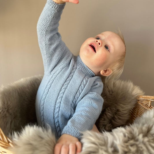 Vesleskattens flettebody i 100% kløfri merinoull med flettemønster – strikkepakke body til baby. Elastisk hals, ingen knapper i halsen og knapper mellom beina for enkelt bleiebytt. Størrelser fra nyfødt til 2,5 år.