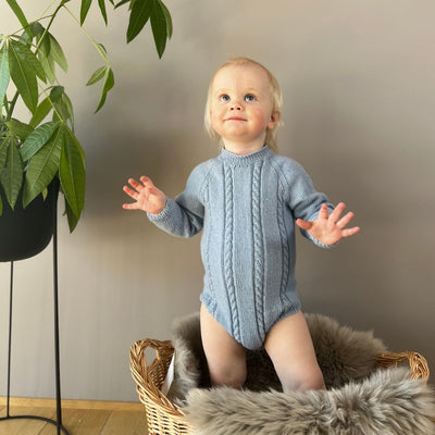 Vesleskattens flettebody på baby – strikkepakke body i 100% kløfri merinoull med flettemønster. Størrelser fra nyfødt til 2,5 år, elastisk hals og knapper mellom beina for enkelt bleiebytt. Enkel av og påkledning.
