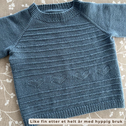 Nærbilde av rillemønster og hjerter på drømmegenser – del av Vesleskattens drømmesett i 100% kløfri merinoull. Strikkepakke genser og lue til baby og barn 0–3 år. Nydelig detalj, perfekt for aktive barnehagebarn.
