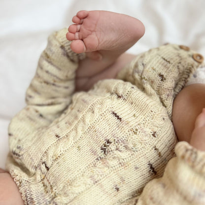 Detaljer forfra på Vesleskattens flettebody – strikkepakke baby i håndfarget eksklusivt Unikt Garn med flettemønster. Størrelser nyfødt til 2,5 år, knapper mellom beina for enkelt bleiebytt.