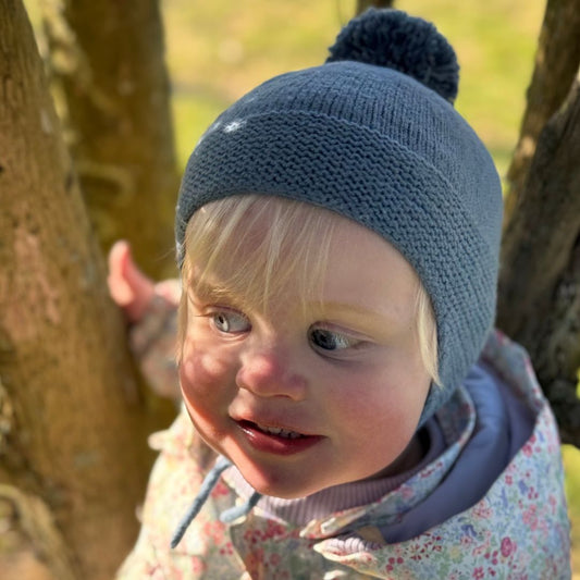 Barn leker i skogen med strikket drømmelue – perfekt lue for aktive barn i 100% kløfri merinoull. Strikkepakke drømmelue med dusk, ørelapper og knyttesnor – den beste lua for barnehage. Nybegynnervennlig strikkeoppskrift for høst og vinter.