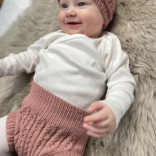 Vesleskattens eventyrbloomer fra siden på baby – bloomer i 100% kløfri merinoull som kan brukes rett på huden. Praktisk under kjoler og fin til nyfødtbilder. Strikkepakke nyfødtstrikk, størrelser 0–1 år.