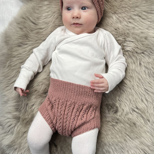 Vesleskattens eventyrbloomer på baby på saueskinn – bloomer i 100% kløfri merinoull, fin til nyfødtbilder. Kan brukes som sperrelag til tøybleier og rett på huden. Strikkepakke nyfødtstrikk, størrelser 0–1 år.